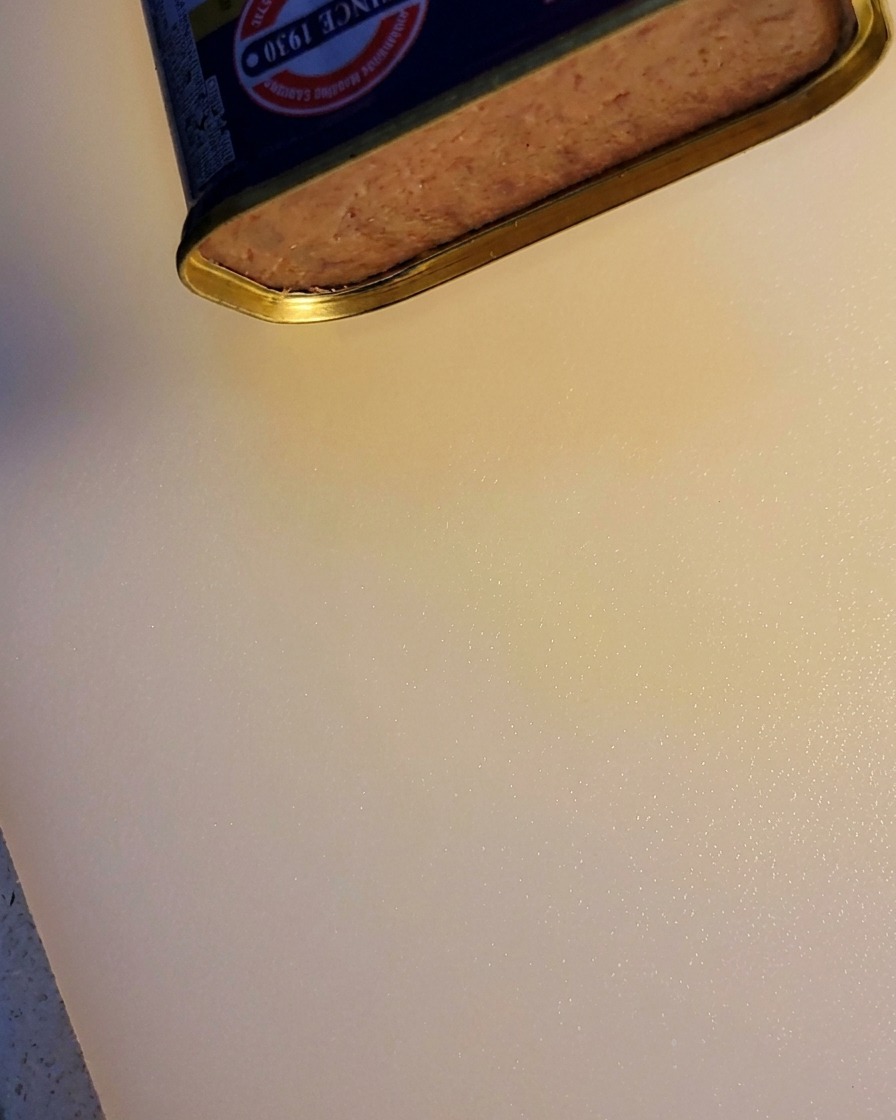 A portion of a luncheon meat block being sliced from the can.