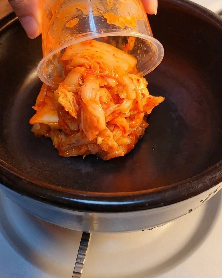 Fermented kimchi and crushed luncheon meat layered in a stone pot.