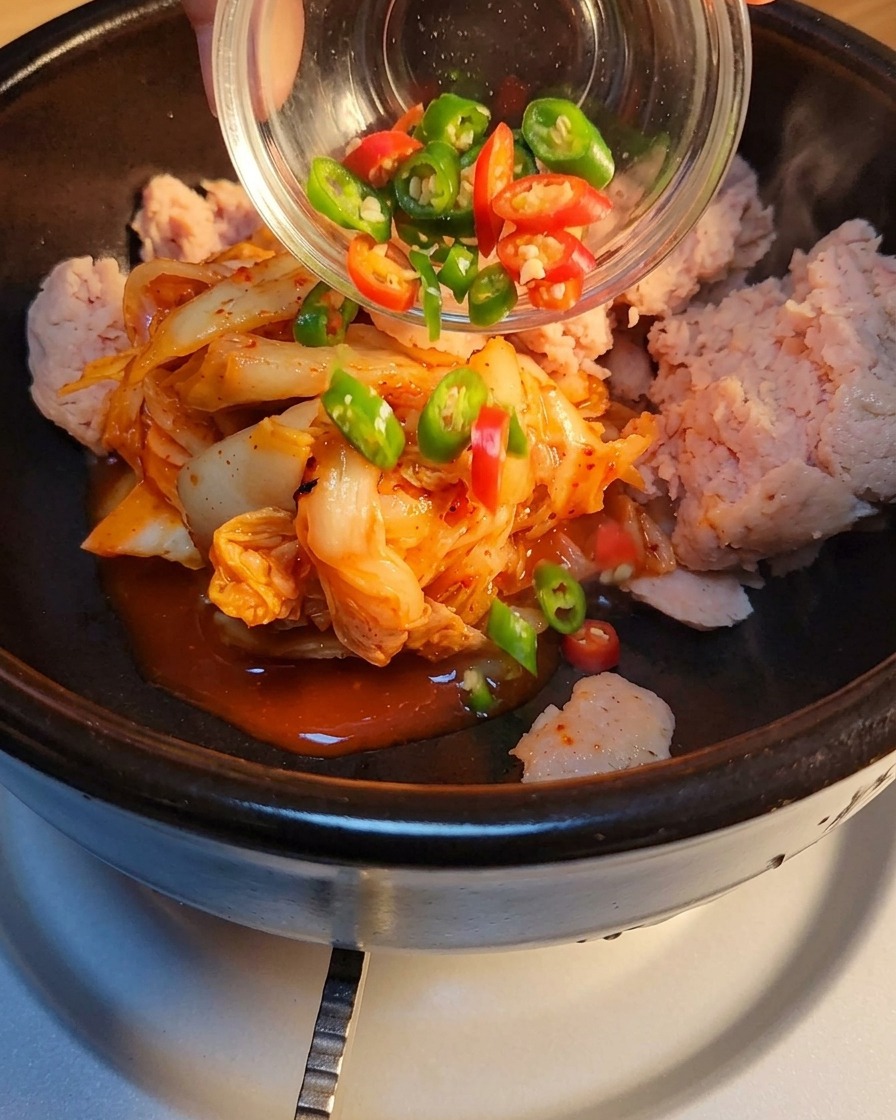 Sliced green and red chilies being added to the stone pot.