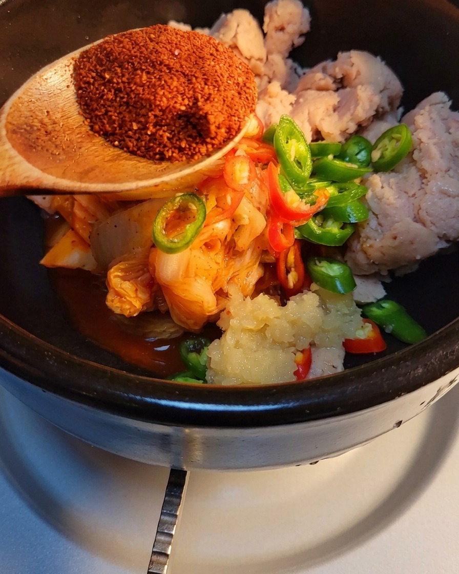 Korean chili powder being spooned onto the other ingredients in the stone pot.