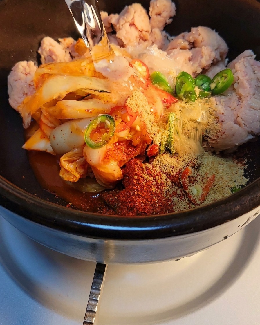 Water being poured into the stone pot with kimchi and spices, ready to be heated on the stove.