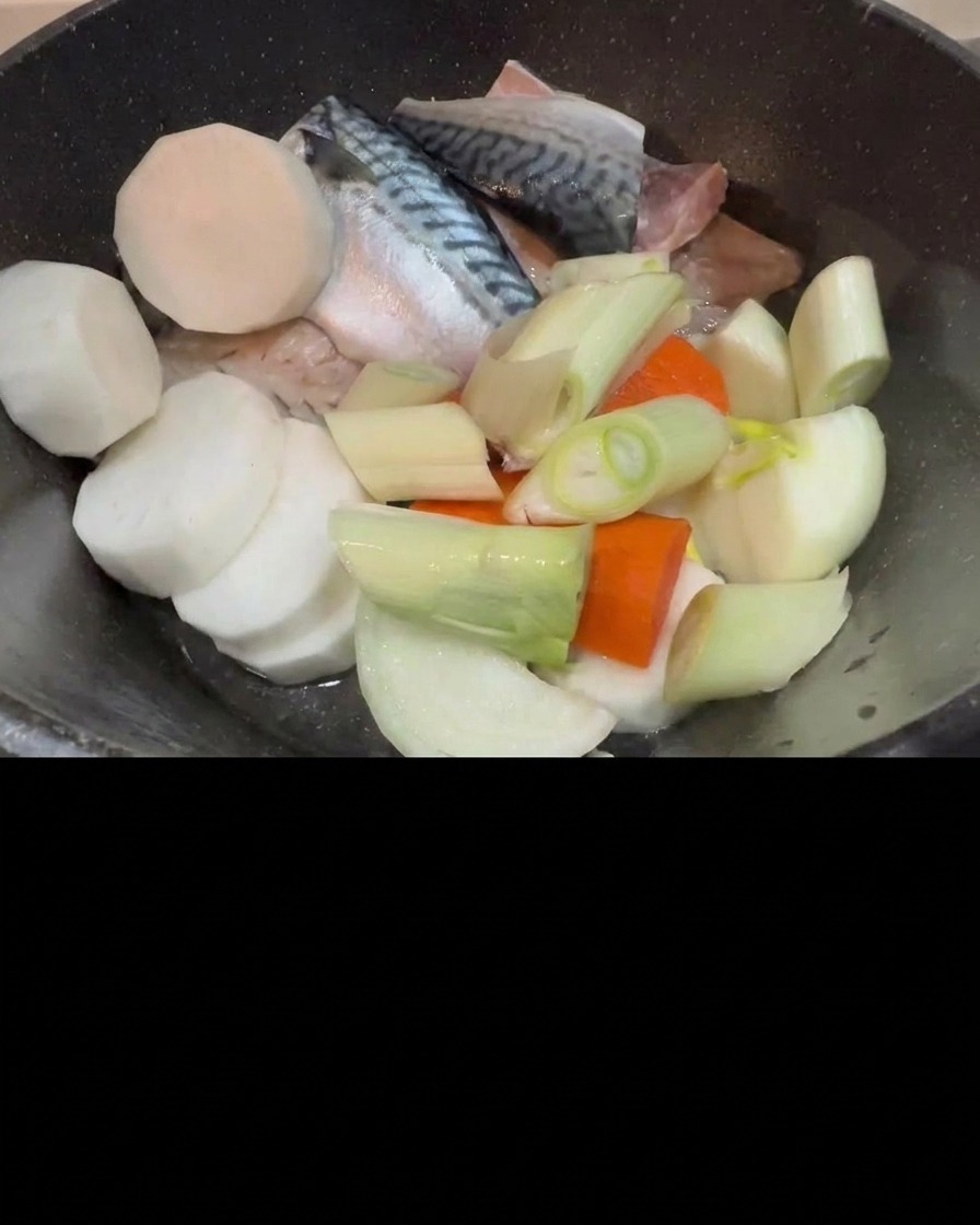 Kimchi being added to the pot of raw mackerel, radish, and green onions.