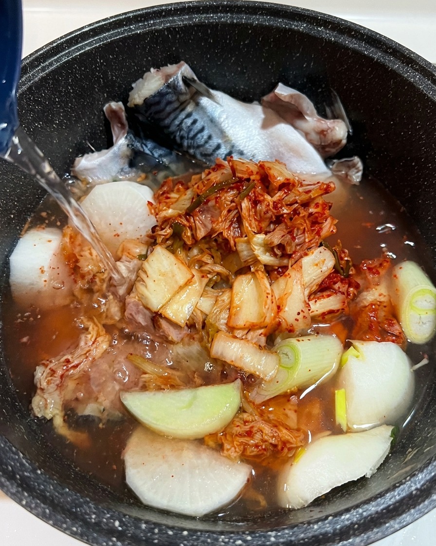 A close-up view of liquid seasoning being added to the pot, with ingredients clearly visible underneath the water.