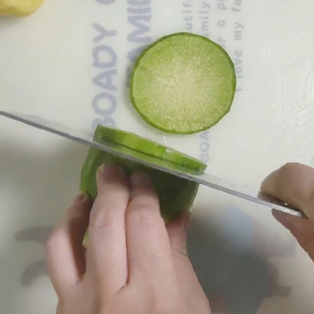 Fresh radish being sliced into thick rounds on a clean white cutting board.