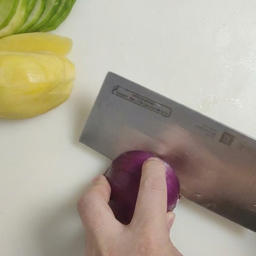 A sharp knife cutting a red onion into large, coarse chunks on a cutting board.