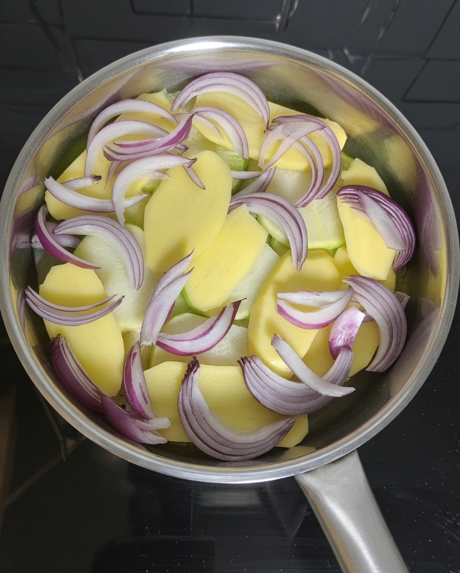 Pieces of canned mackerel being arranged on top of potato and onion slices in a pot.