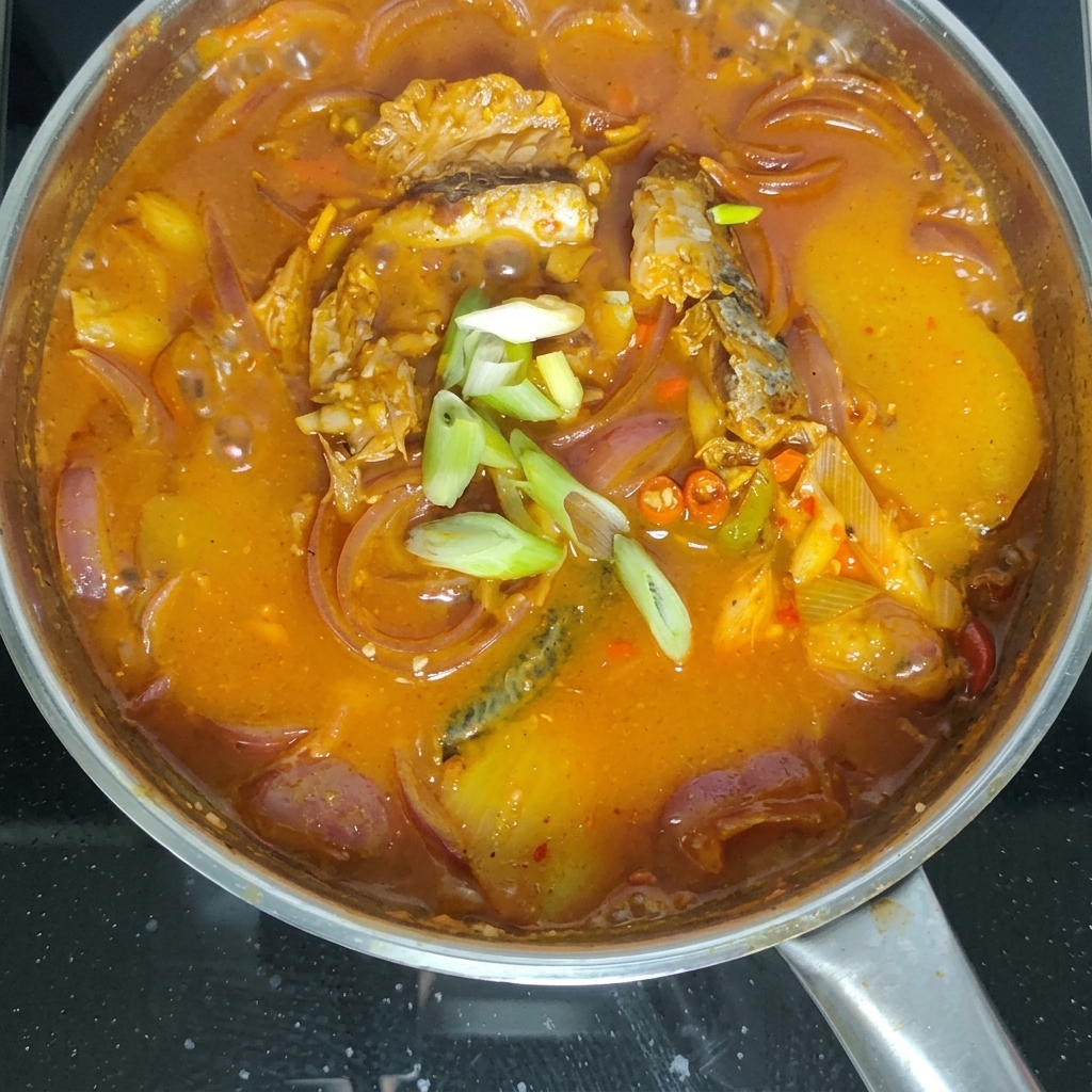 Green onion sections being scattered over the top of the bubbling mackerel stew.