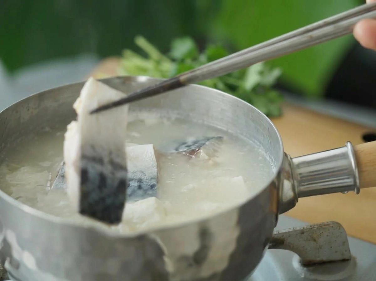 Pieces of blanched mackerel being lowered into the boiling soup with chopsticks.