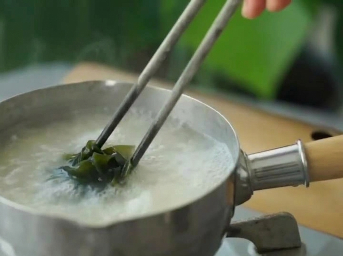 Rehydrated green wakame being added to the simmering miso soup using chopsticks.