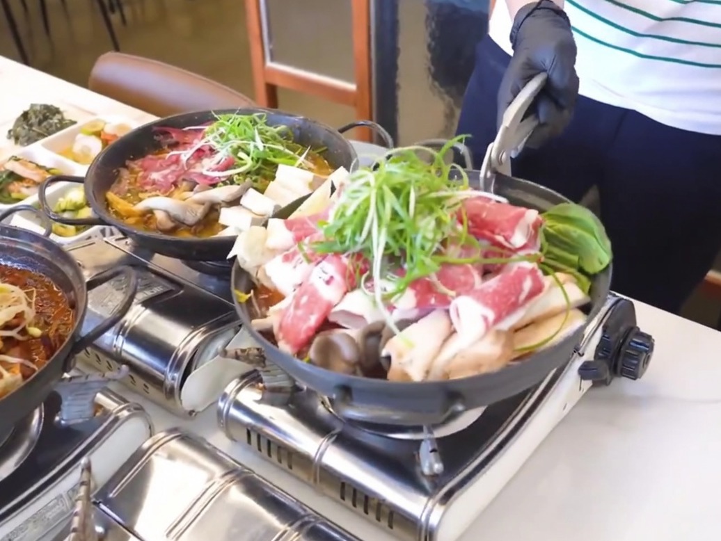A black iron pan being prepared with a layer of cooked radish and kimchi at the bottom.