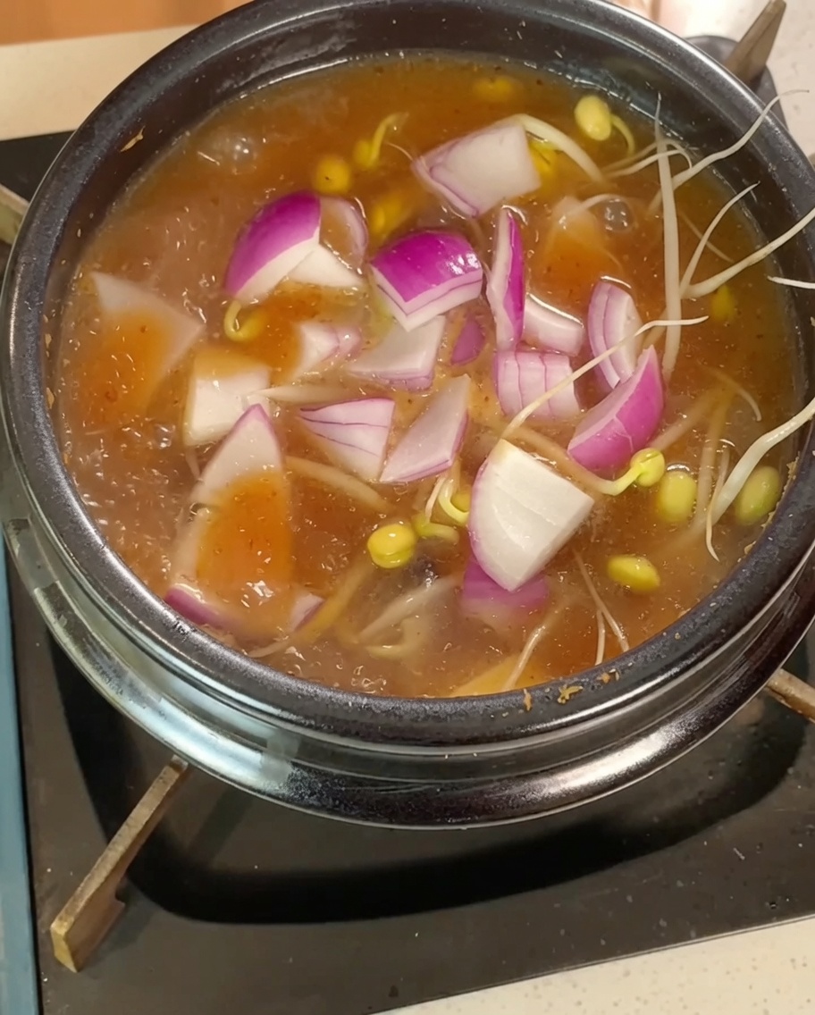 Bean sprouts, red onion slices, and cubed tofu simmering in the boiling broth.