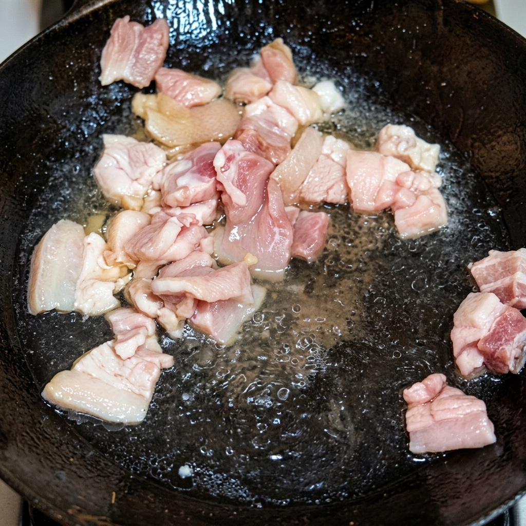 Golden brown pork belly pieces frying in rendered lard in a traditional wok.