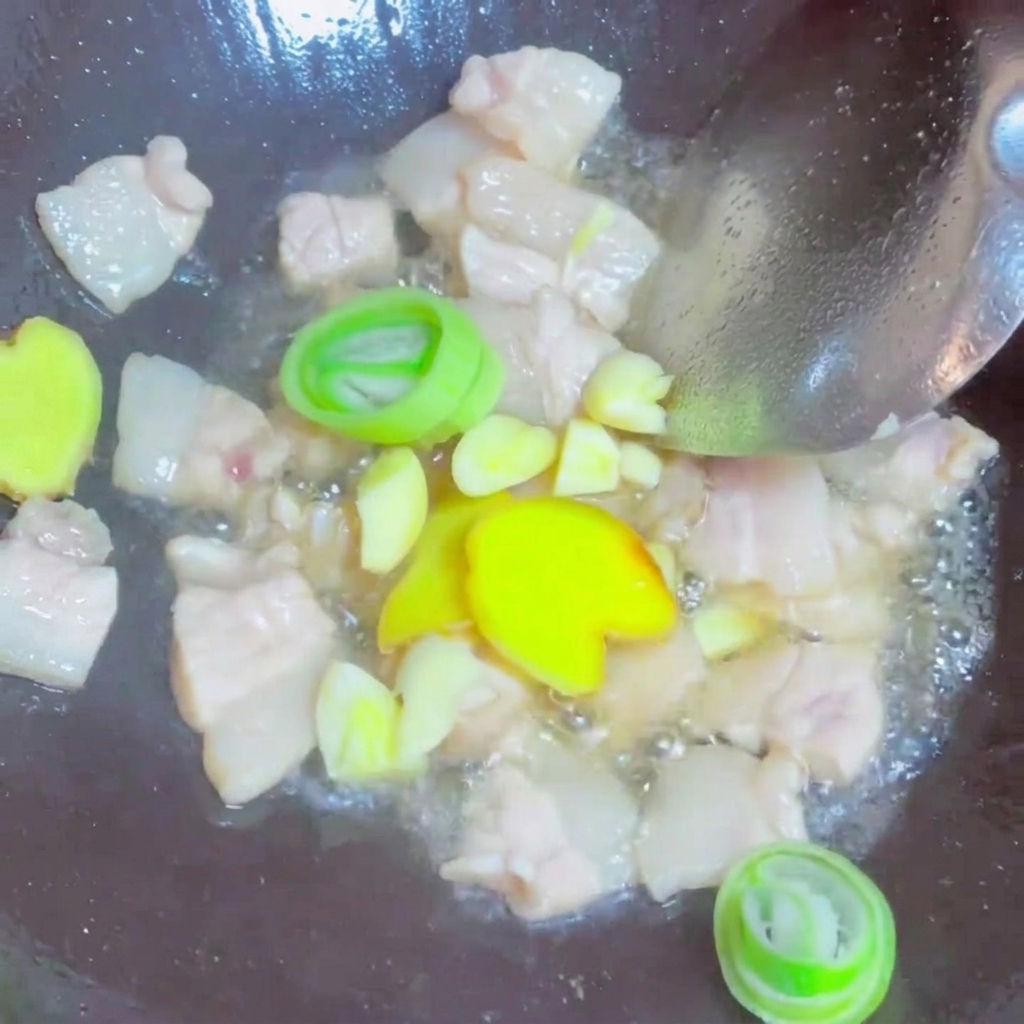 Slices of fresh ginger, garlic, and green scallion rings being tossed with fried pork pieces in a wok.