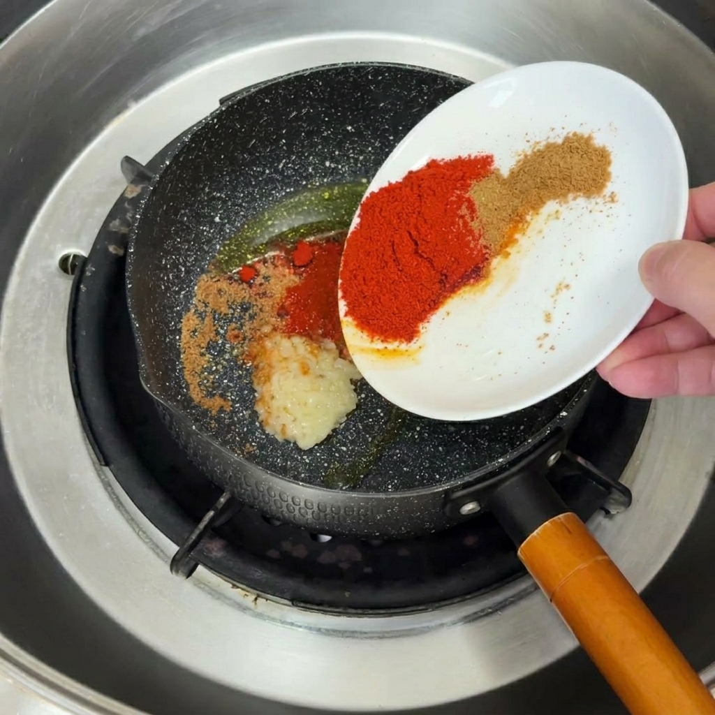 Minced garlic and spices sizzling and browning in hot oil within a black frying pan.