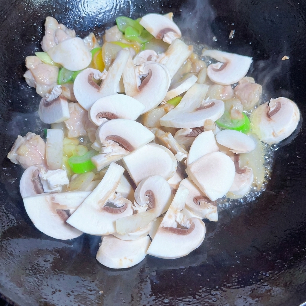 A mixture of sliced mushrooms, onions, and bean sprouts being stirred in a pan with spices.