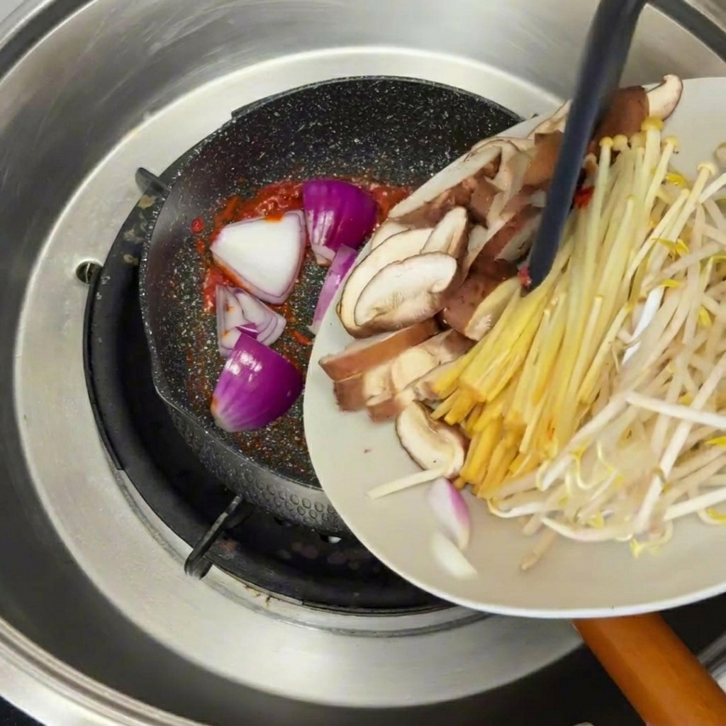 Sesame oil being poured from a spoon into a pot of boiling, aromatic beef and tofu stew.
