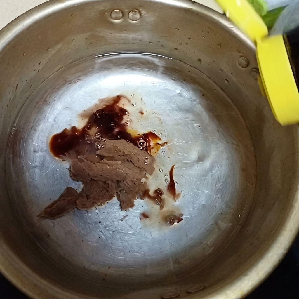 Oyster sauce and a dash of fish sauce being poured into the metal pot over the soybean paste.