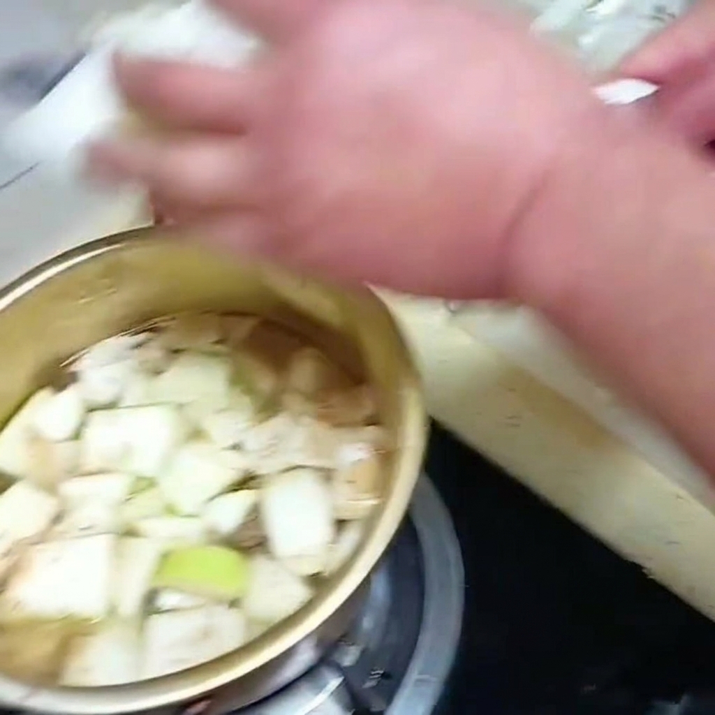 Sliced Napa cabbage leaves being placed into a simmering pot of soup with other vegetables.