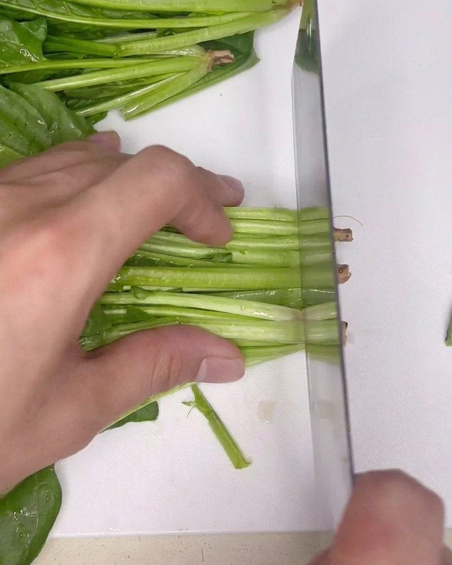 Fresh bunch of green spinach on a clean white cutting board, ready to be trimmed with a knife.