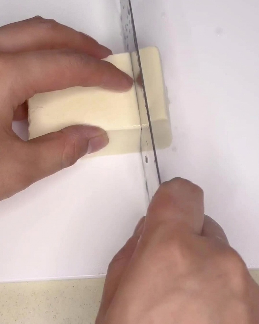 Firm white tofu block being sliced into small rectangles with a large kitchen knife on a cutting board.