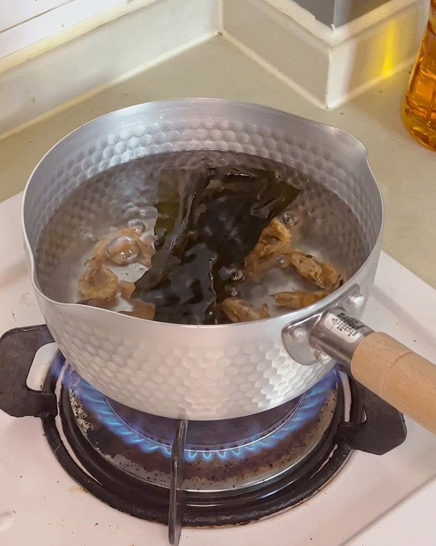 Close-up of dried shrimp and a dark piece of dried kelp submerged in the water inside a cooking pot.