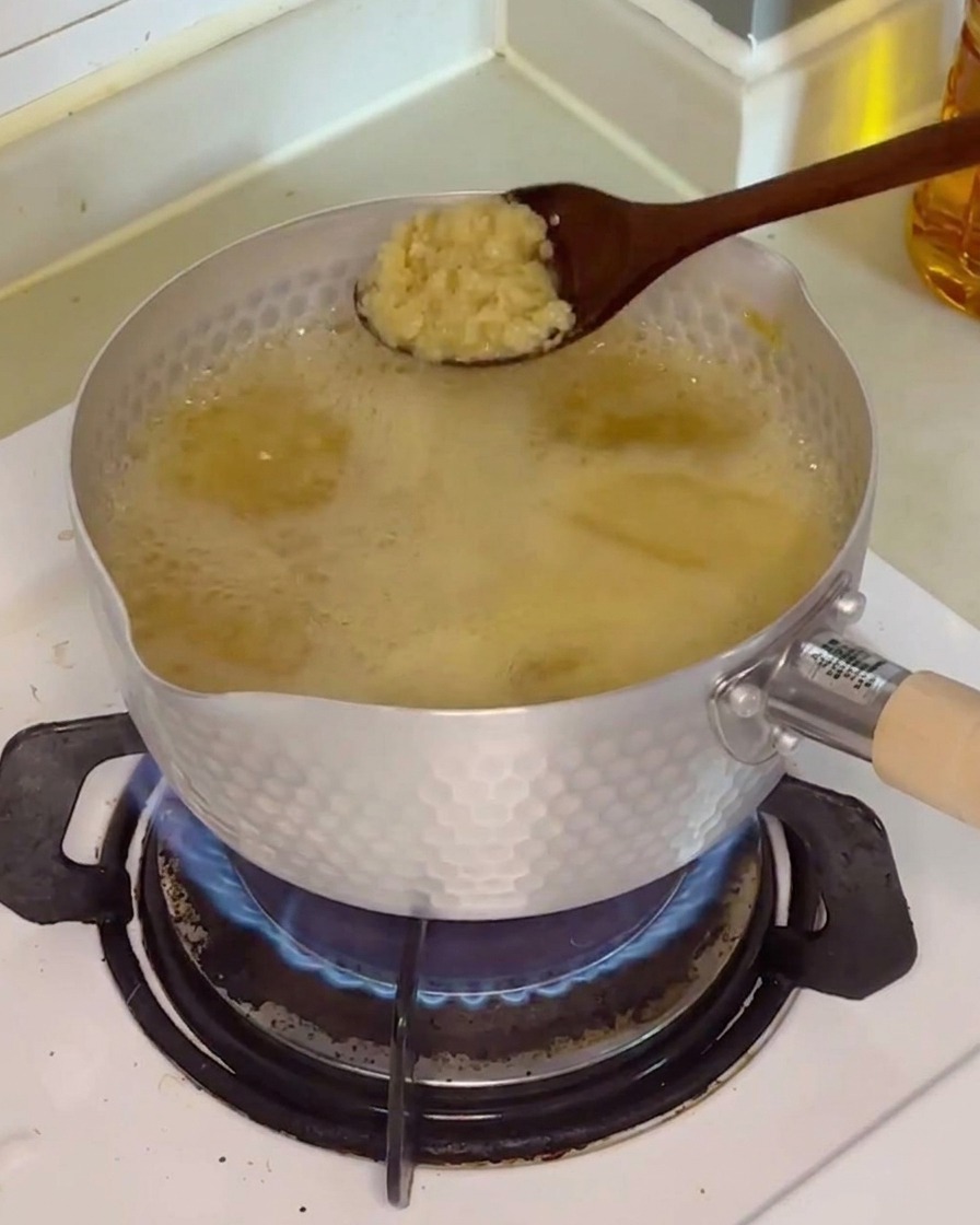 A spoonful of fresh minced garlic being dropped into the simmering, light brown broth.