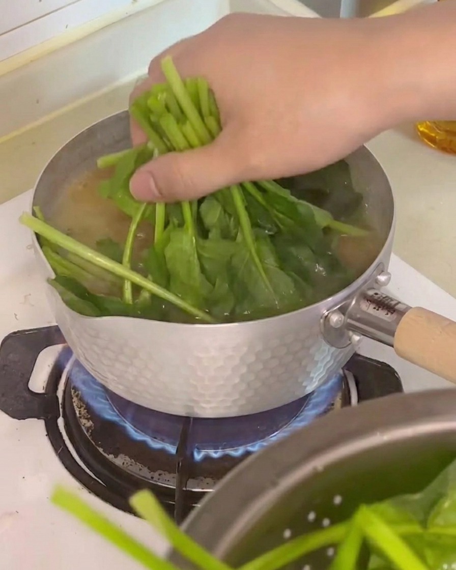 Fresh spinach, tofu cubes, and enoki mushrooms being added to the simmering soup pot.