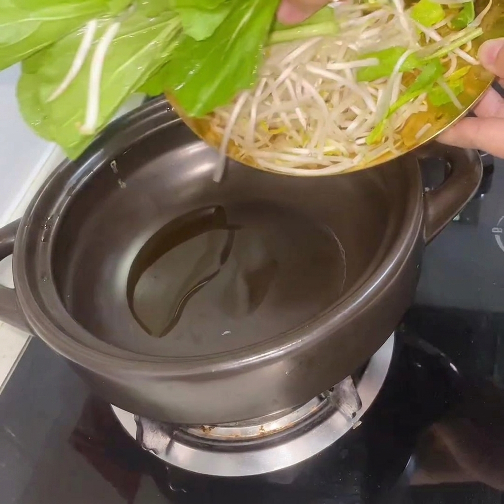 Fresh bok choy and bean sprouts being stirred in the heated clay pot.