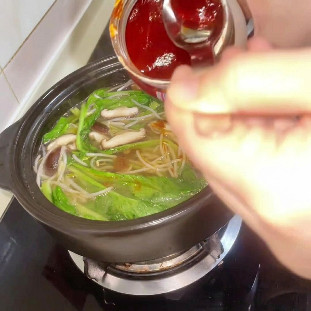 Korean chili paste being added to the stew, with the broth being stirred.