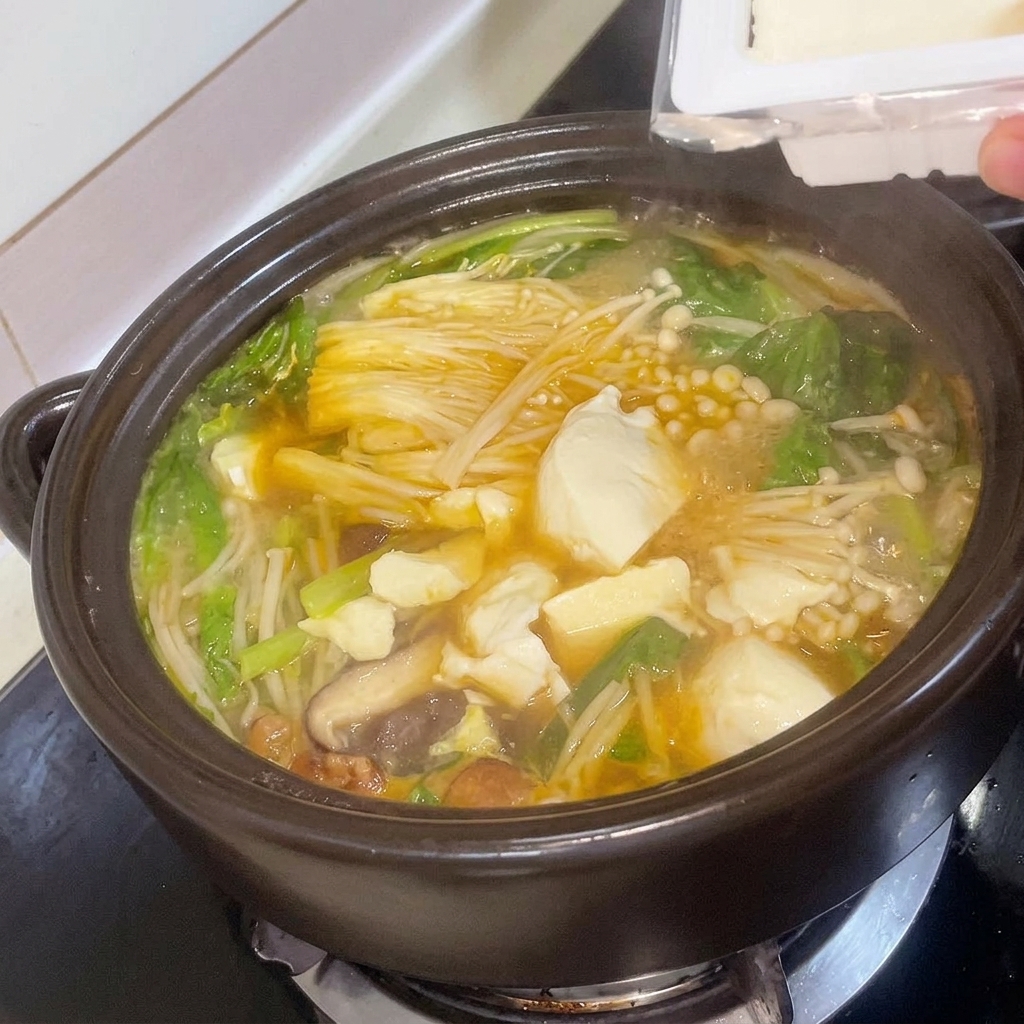 Fresh tofu cubes being carefully added to the simmering Korean soybean paste stew in a clay pot.