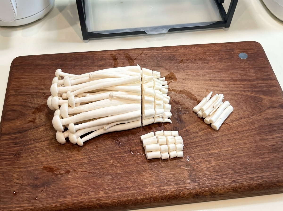 Fresh seafood mushrooms on a wooden cutting board with the root ends being trimmed off by a knife.