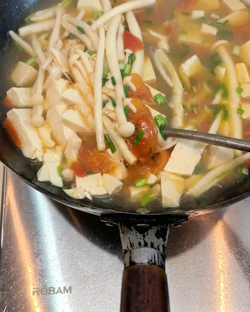 Tomatoes cooking in a wok with melted lard, starting to soften and release juices.