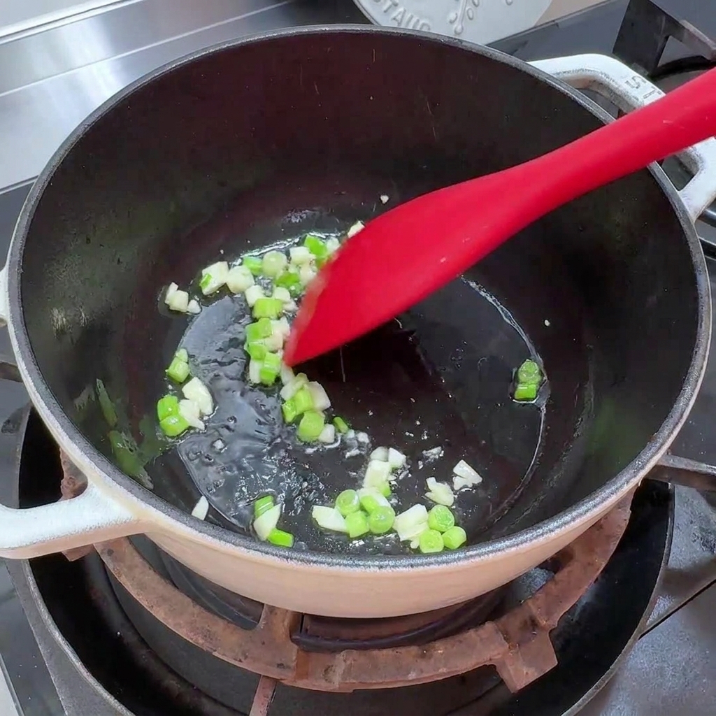 Chopped green onions and minced garlic sizzling in a small amount of oil in a pot.