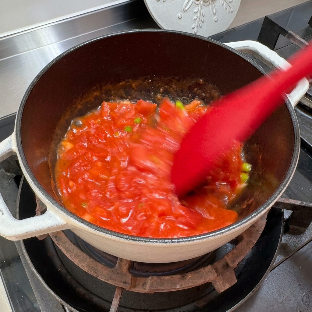 Tomatoes being mashed and stirred in a pot to create a sauce-like consistency.