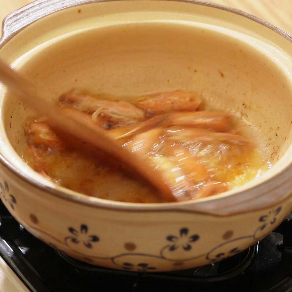 Hot water being poured into a clay pot with sautéed shrimp heads.