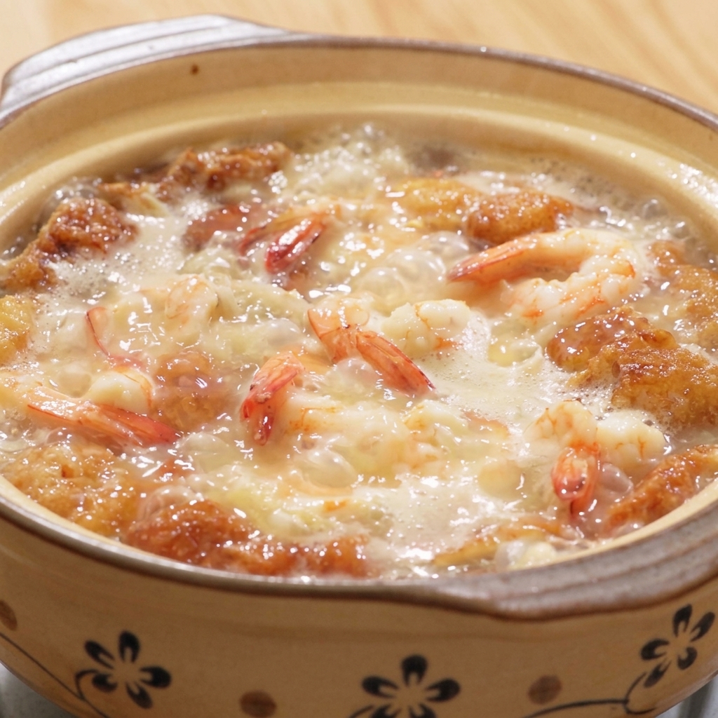 A steaming clay pot of soup with shrimp, tofu, and eggs, being seasoned with white pepper and salt.