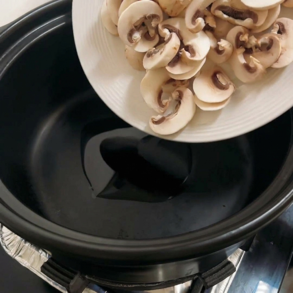 Sliced portobello mushrooms cooking in a black pot, turning golden brown.