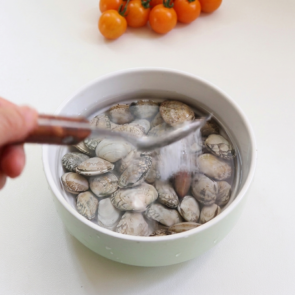 Clams submerged in a bowl of water with a spoonful of salt being added.
