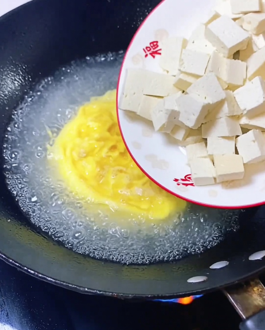 Tofu cubes being added to the simmering egg broth.
