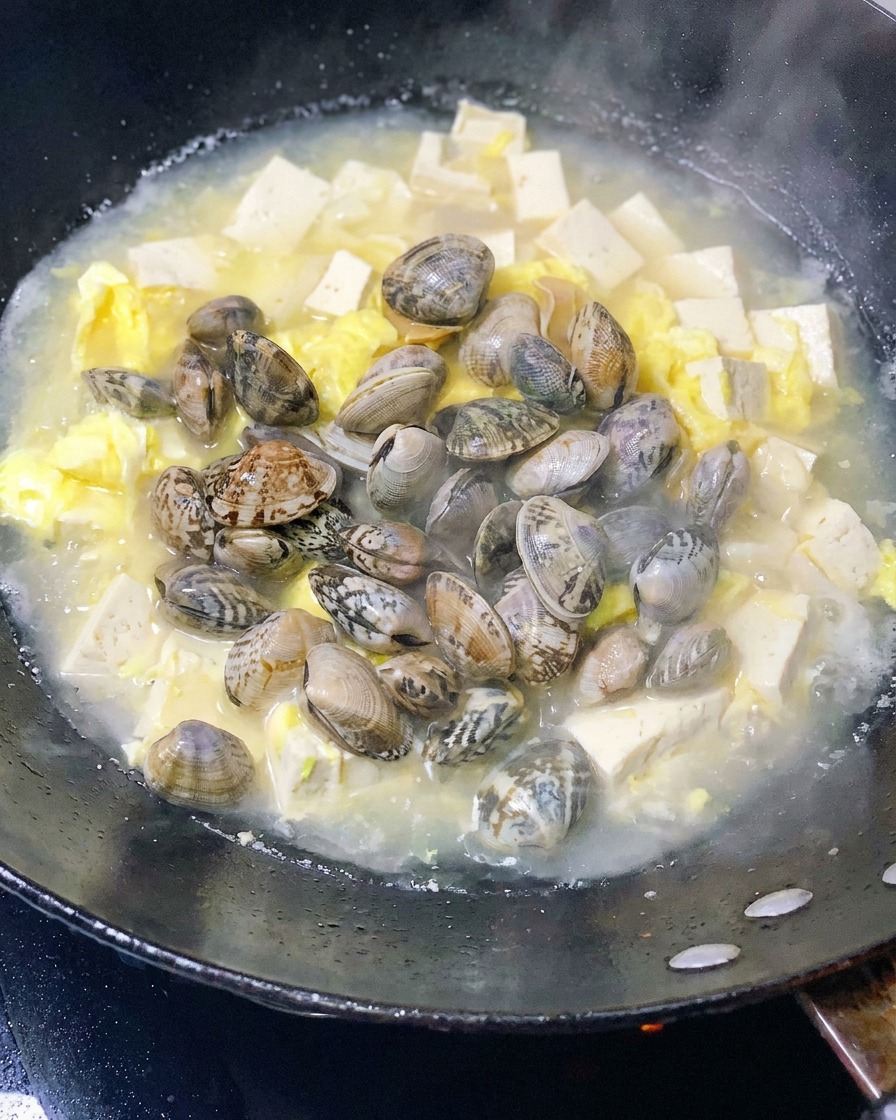 Fresh clams added to the pot with simmering tofu and eggs.