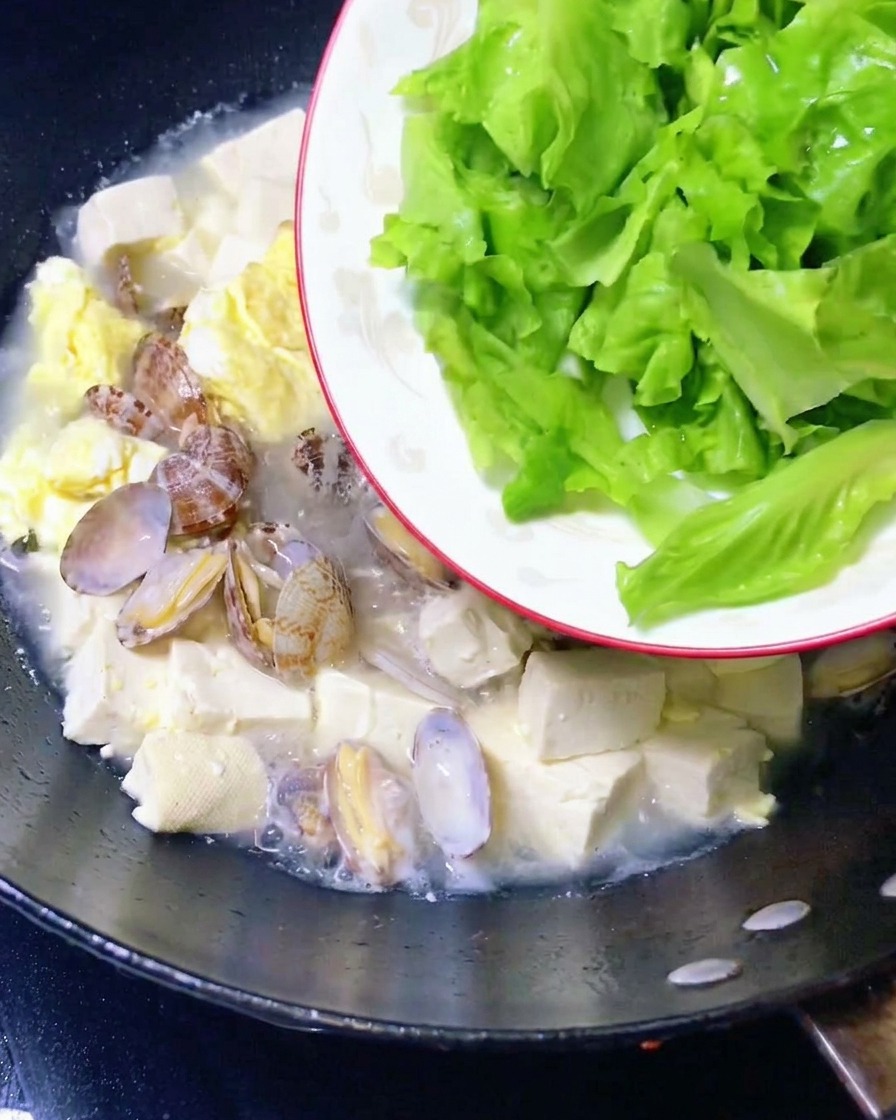 Lettuce leaves being added to the finished clam and tofu stew.