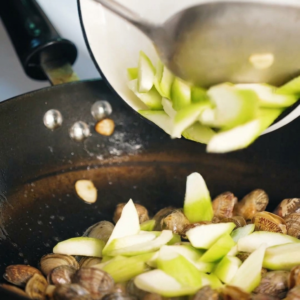 Sliced luffa being stir-fried with clams in the pan.