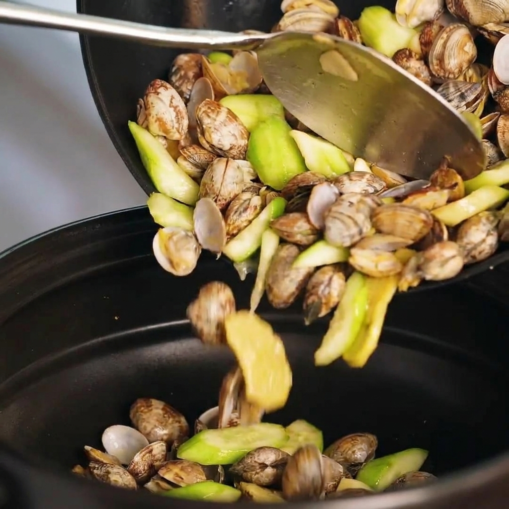 Stir-fried mixture of clams and luffa being transferred into a clay pot.