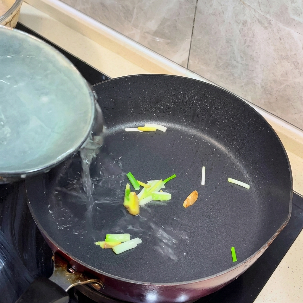 Boiling water being poured into a pan with sautéed ginger and scallions.