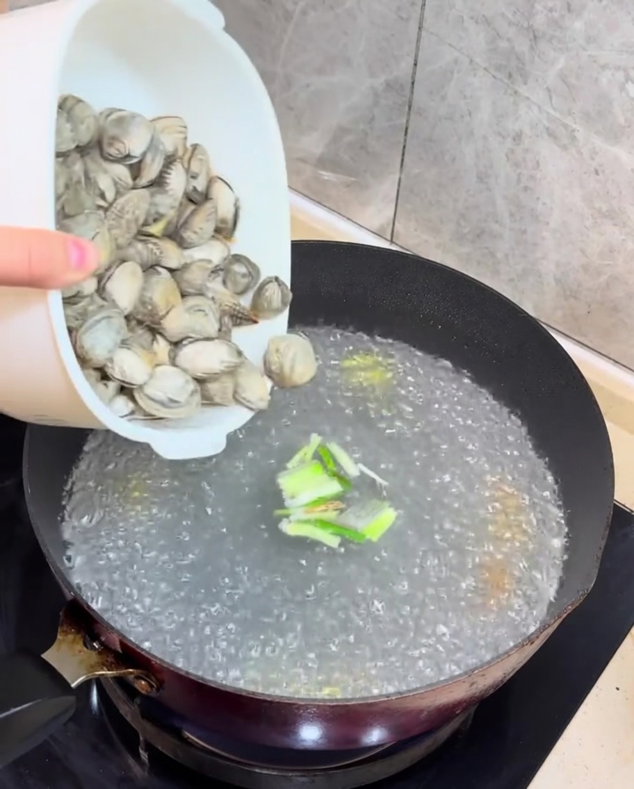 Fresh clams and cubed tofu being added to the boiling broth.