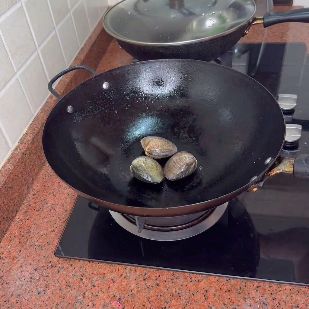 Three closed clams sitting in a black wok on a stovetop.