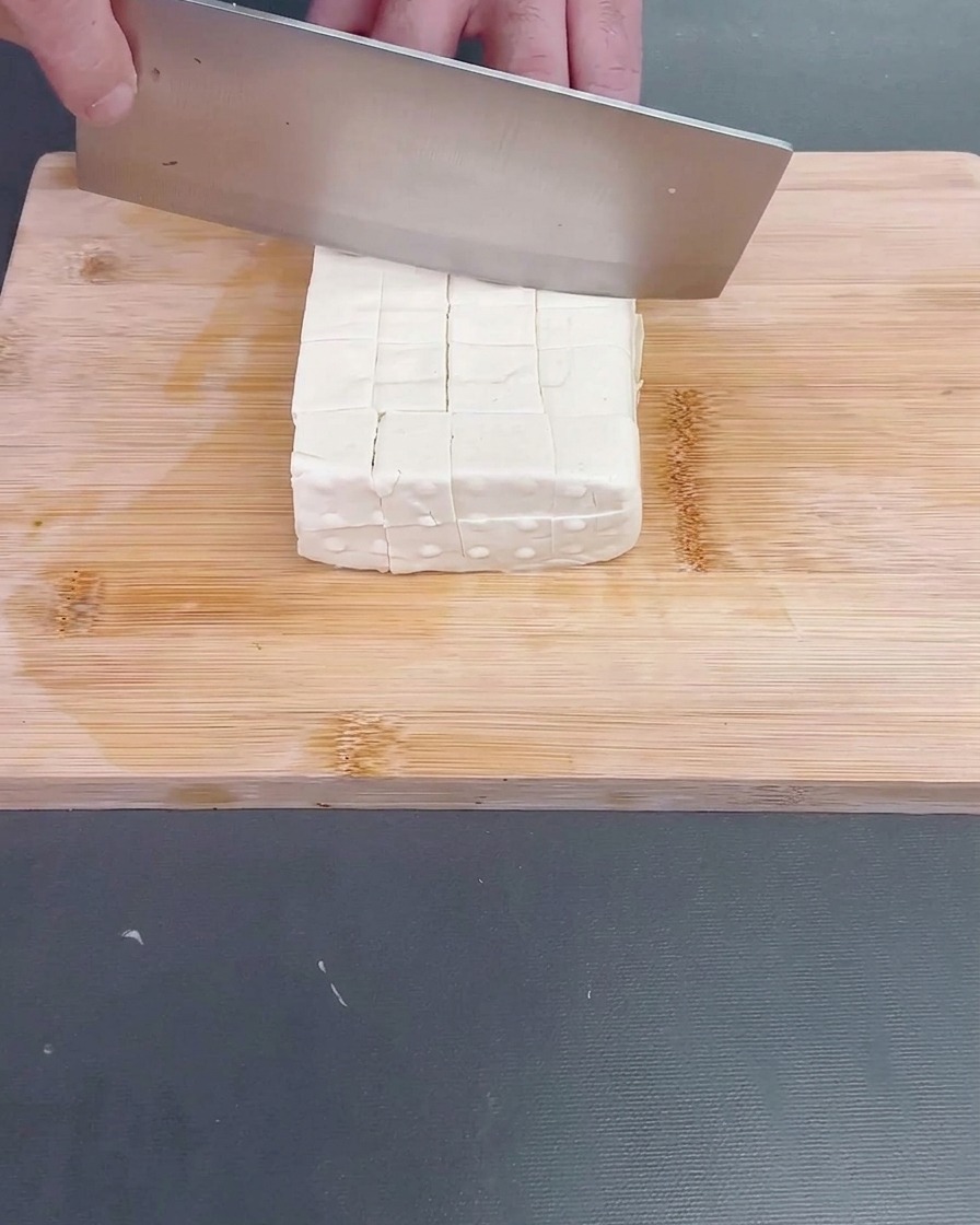 A freshly peeled luffa being cut into irregular, bite-sized rolling chunks.