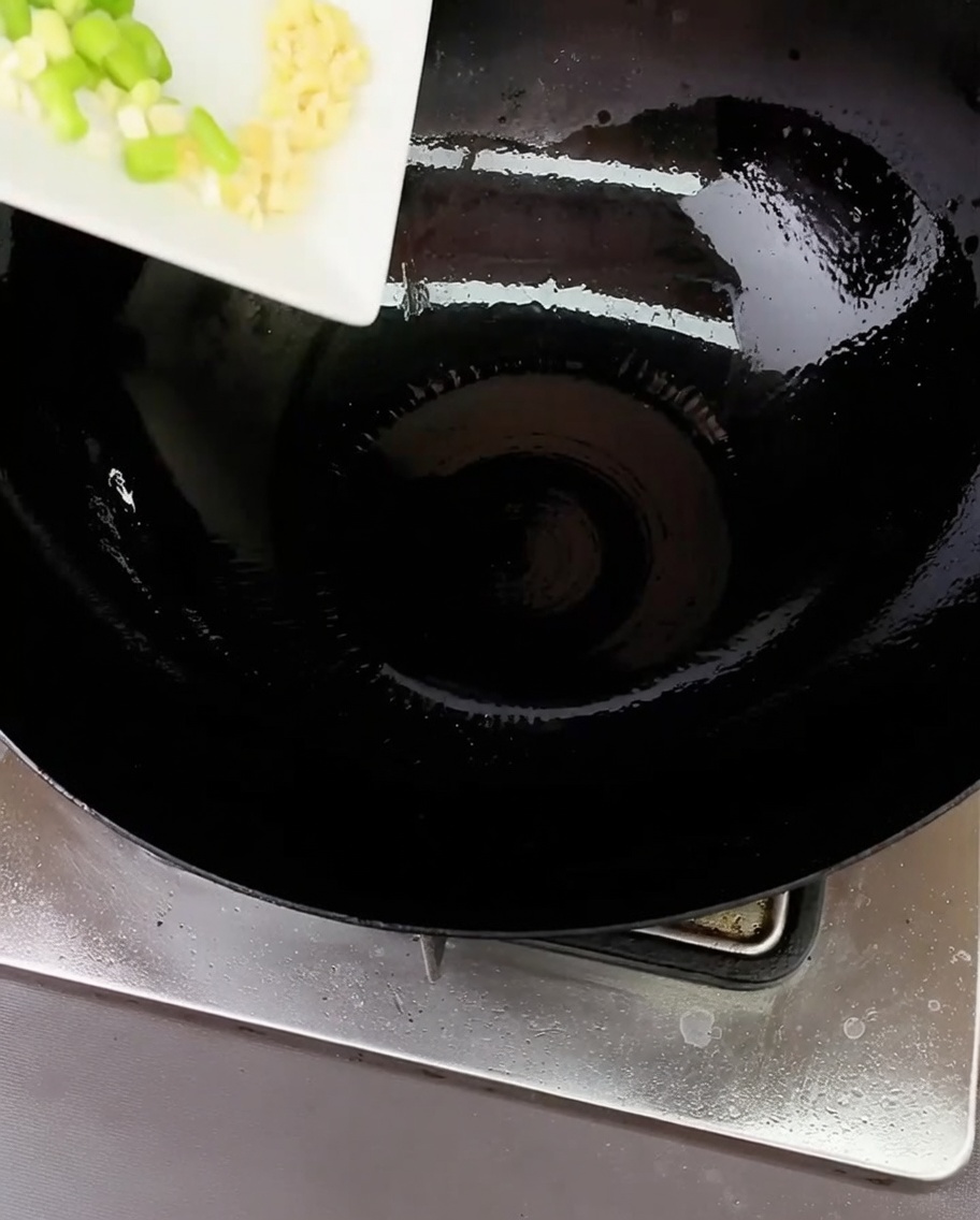 Chopped green onions and minced garlic sizzling in a hot wok with a small amount of oil.