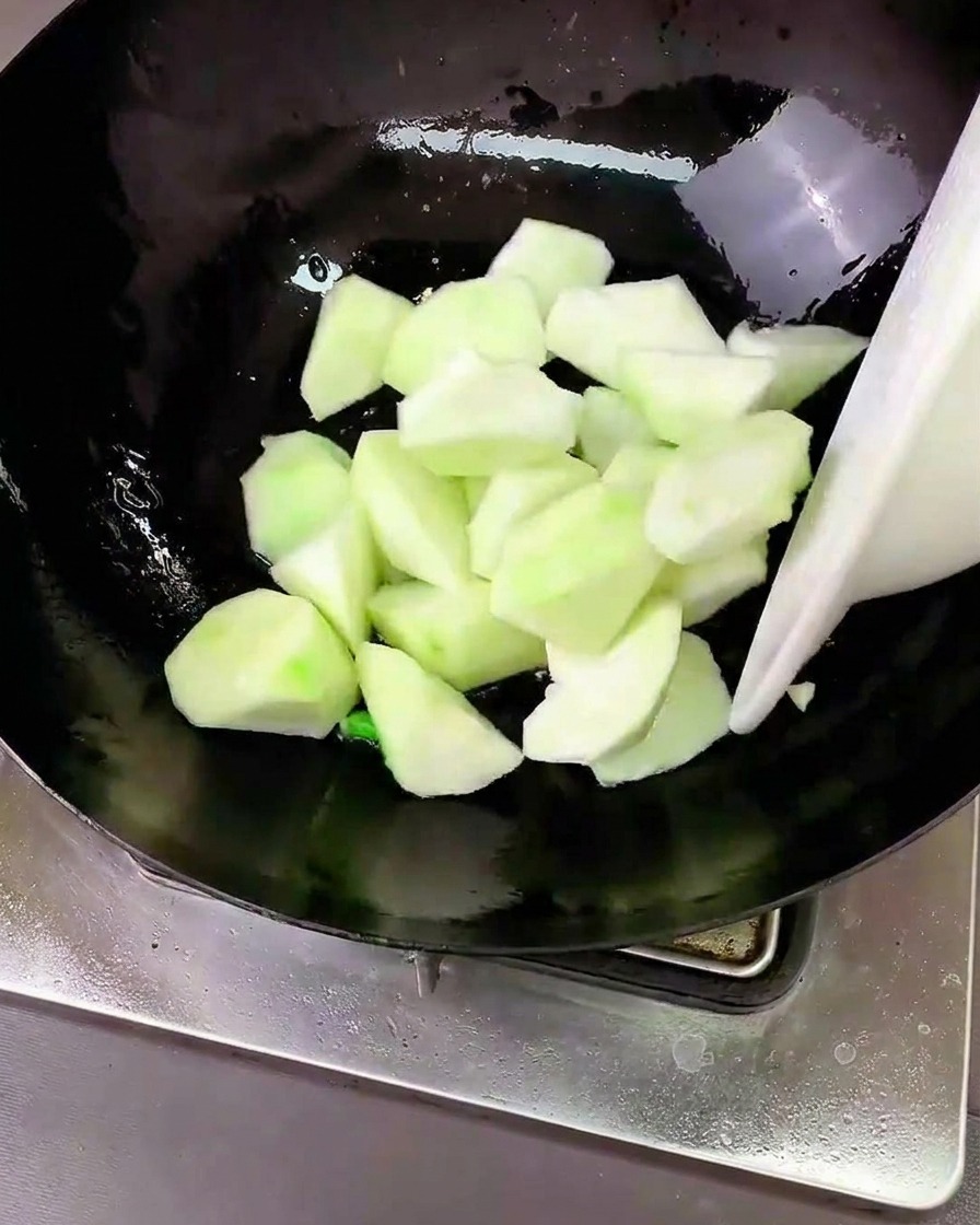 Luffa chunks being stirred in a wok with sautéed aromatics.