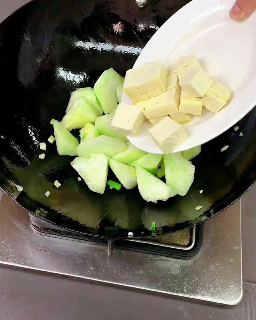 Fresh tofu cubes and clean, raw clams being added to the wok with the luffa.